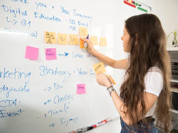 A teacher is brainstorming ideas for her course by placing post it notes on a white board